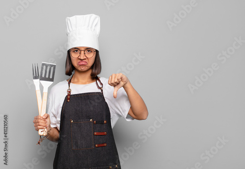 young hispanic woman feeling cross, angry, annoyed, disappointed or displeased, showing thumbs down with a serious look photo