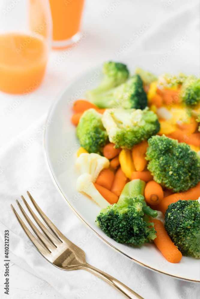 Mixed broccoli, cauliflower, carrot on a plate and a golden fork on light background Mixed broccoli, cauliflower, carrot on a plate and a golden fork on light background