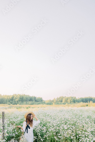 Beautiful woman enjoying daisy field, nice female lying down in meadow of flowers, pretty girl relaxing outdoor, having fun, holding plant, happy young lady and spring green nature, harmony concept © NEZNAEV