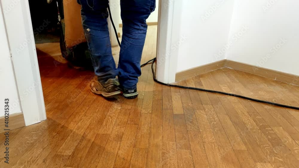 Worker man sanding wooden floor of parquet, with pad sander machine in an empty room during a renovation. Sand and refinish hardwood floors. Worker man sanding wooden floor of parquet, with pad sander machine in an empty room during a renovation. Sand and refinish hardwood floors.