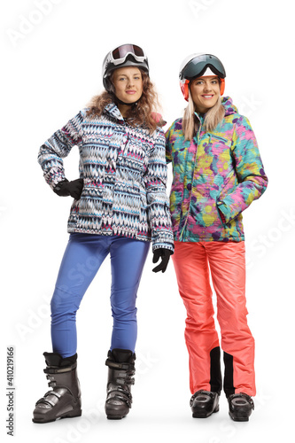 Full length portrait of a two female friends in ski uniforms smiling and looking at the camera