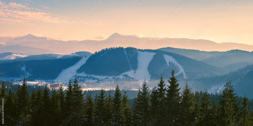A Scenic view on a ski resort during a warm sunset in winter with a snowy mountain ridge in behind