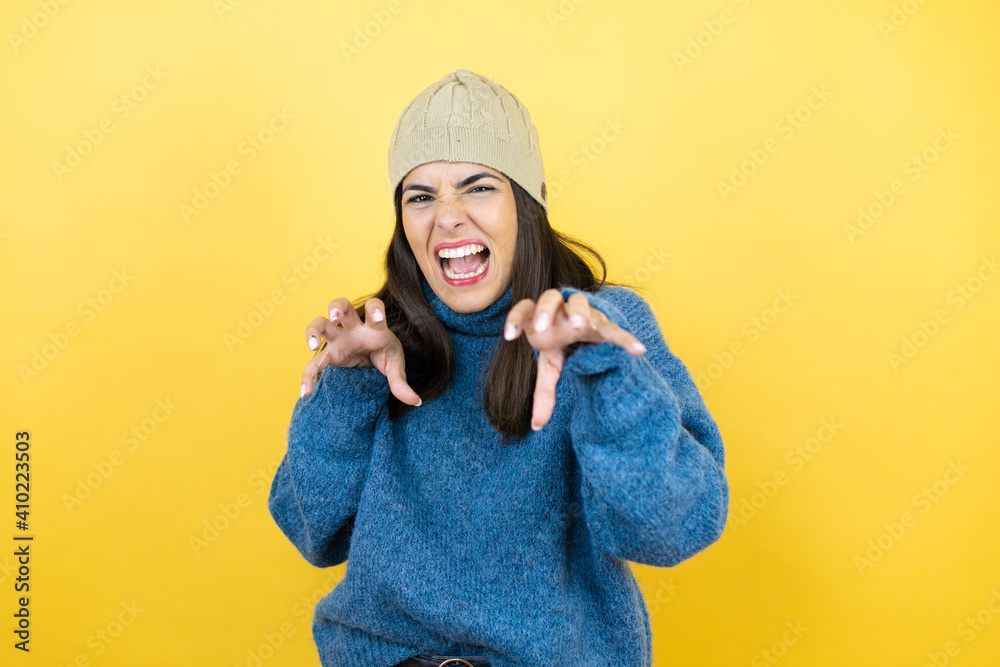 Young beautiful woman wearing blue casual sweater and wool hat smiling funny doing claw gesture as cat, aggressive and sexy expression