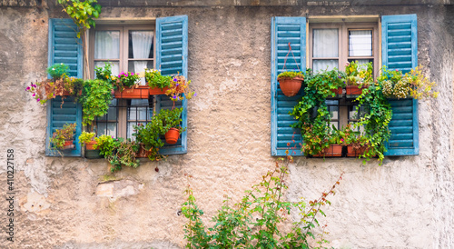 Vintage, traditional italian house wall with old blue window shutters and many plant pots. Typical european postcard view.