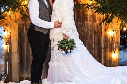 Newlywed couple, bride and groom on the background of an old wooden house and retro garland. Rustic winter wedding.