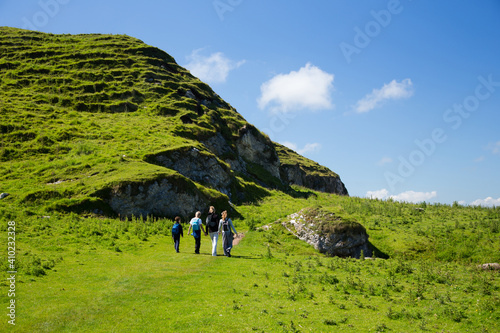 Familiy is hiking, mother and three kids walks along a green grass covered irish land.