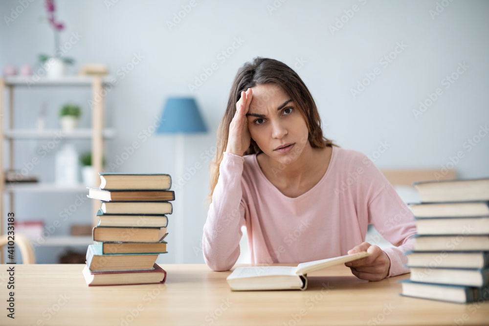 Unhappy woman student sitting at a table with a pile of books. Unhappy woman student sitting at a table with a pile of books.