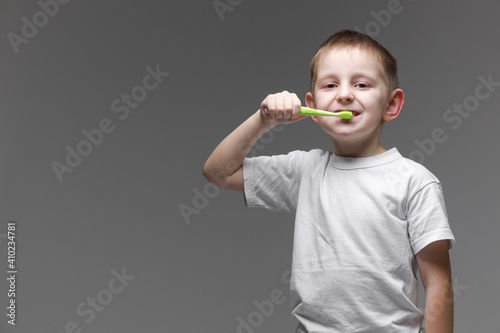 Happy child kid boy brushing teeth with toothbrush on gray background. Health care, dental hygiene. Mockup, copy space photo