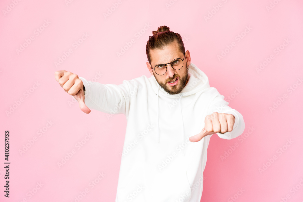 Young man with long hair look showing thumb down and expressing dislike.