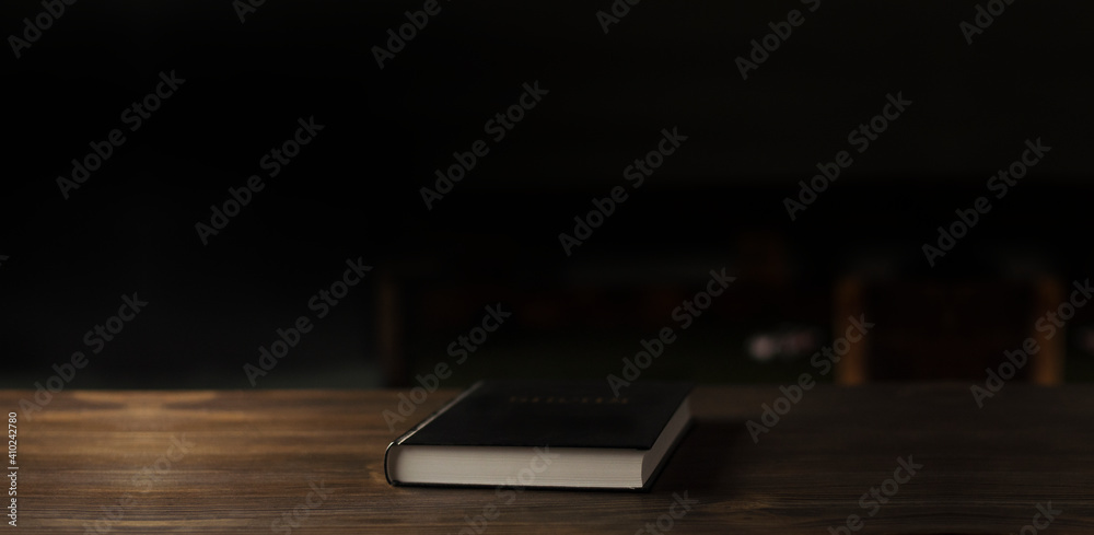 Closed Bible book on a wooden table in the dark. Closed Bible book on a wooden table in the dark.