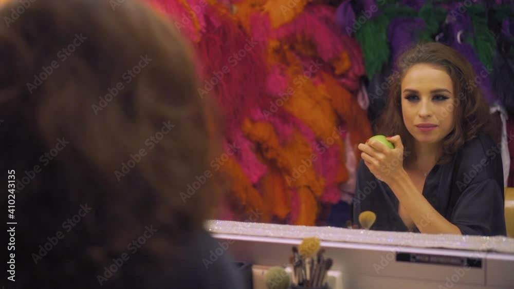 Beautiful girl actress with makeup bites off and eats a green apple in front of the mirror Beautiful girl actress with makeup bites off and eats a green apple in front of the mirror