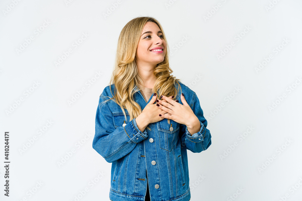 Young caucasian blonde woman has friendly expression, pressing palm to chest. Love concept.