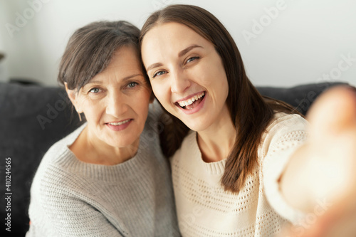 A grown daughter and a senior elderly mother takes a selfie, two smiling multigenerational women looks at the camera cheerfully, record themself photo