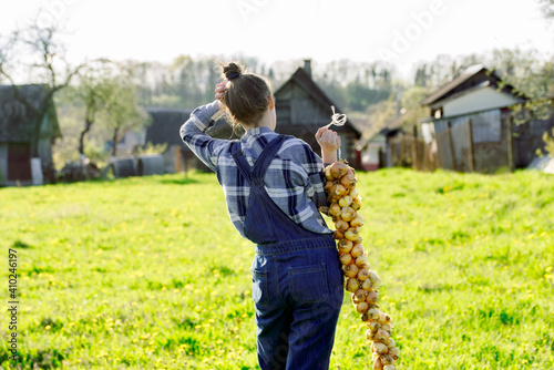 Happy Teenager girl in summer yellow boxing field. Girl farmer preparing for planting bulbs. Bouquet of onions in the hands. Sunny warm day in the village