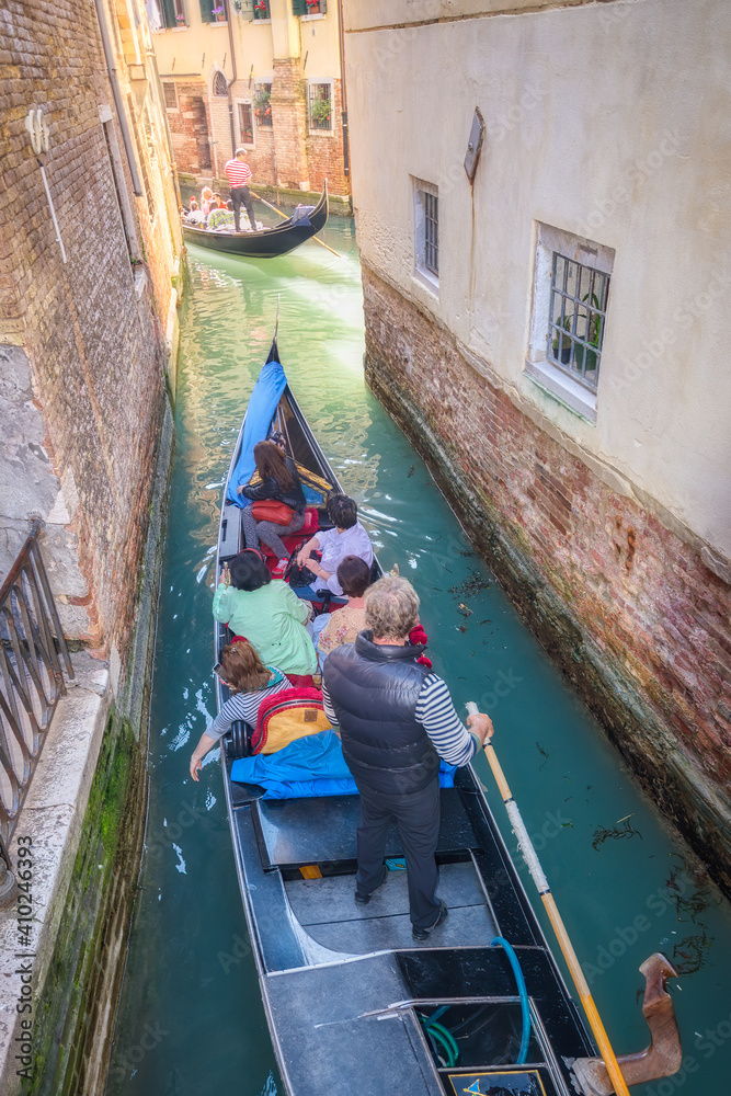 Gondolier carries tourists on gondola in the canals of Venice, Italy.