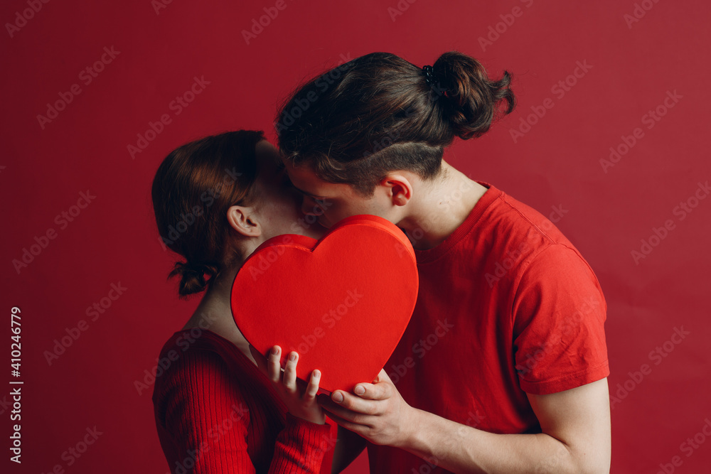 Man and woman young couple kissing and hiding behind heart-shaped box Man and woman young couple kissing and hiding behind heart-shaped box