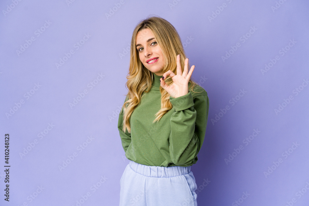 Young caucasian blonde woman winks an eye and holds an okay gesture with hand. Young caucasian blonde woman winks an eye and holds an okay gesture with hand.