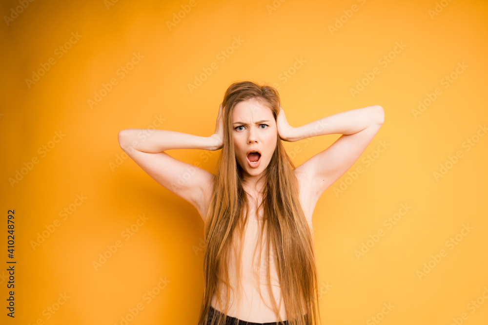 Attractive Caucasian girl with long hair holds her head with her hands and shouts, on an orange background. Emotional woman Attractive Caucasian girl with long hair holds her head with her hands and shouts, on an orange background. Emotional woman
