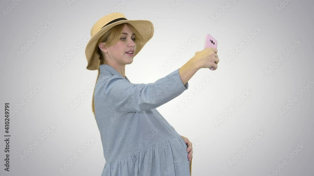 Charming pregnant woman in a hat making selfie on gradient background. Charming pregnant woman in a hat making selfie on gradient background.