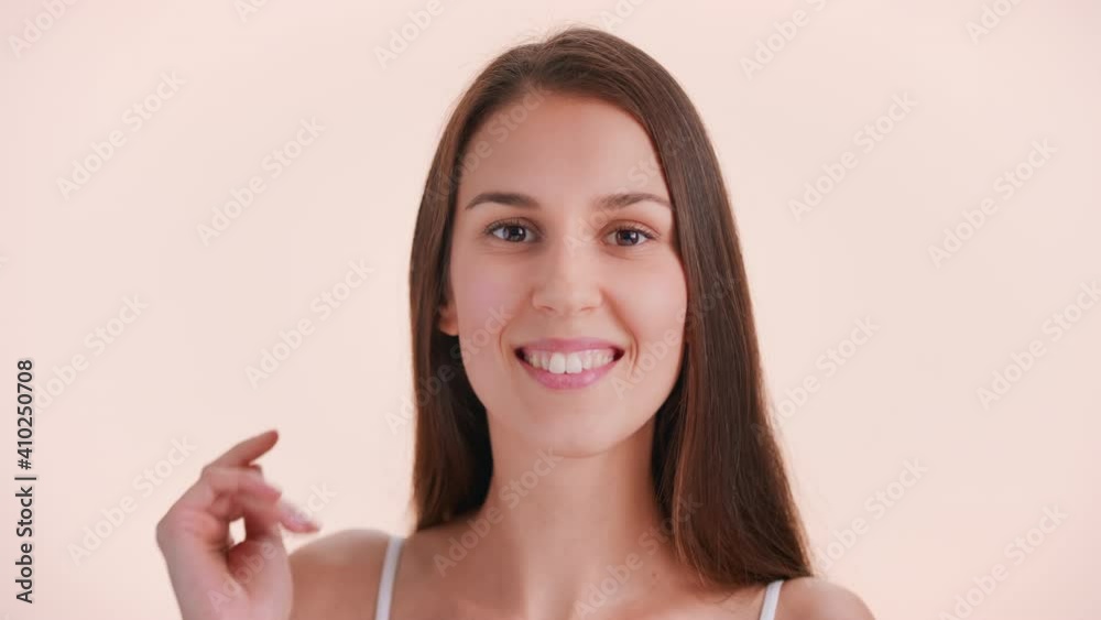 Close-up beauty portrait of young brunette woman with a perfect skin and long hair turns to the camera gently touching her face, looks at camera and smiles Close-up beauty portrait of young brunette woman with a perfect skin and long hair turns to the camera gently touching her face, looks at camera and smiles