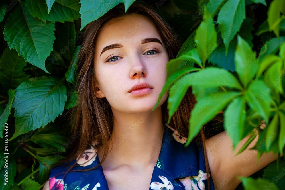 Fototapeta premium Young woman in blue flowers dress on green ivy background