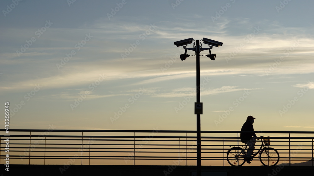 Obraz premium silhouette of cyclist walking down security camera street at sunset