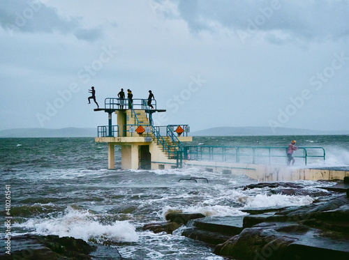 Silhouetted kids jumping off Blackrock diving tower into a stormy sea