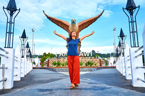 Happy girl tourist posing next to sculpture of a red eagle spreading its wings. Popular tourist spot on Langkawi island