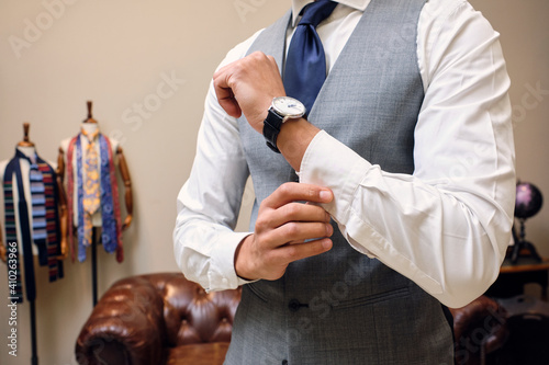 Man in gray waistcoat fastening shirt cuff in tailors boutique photo