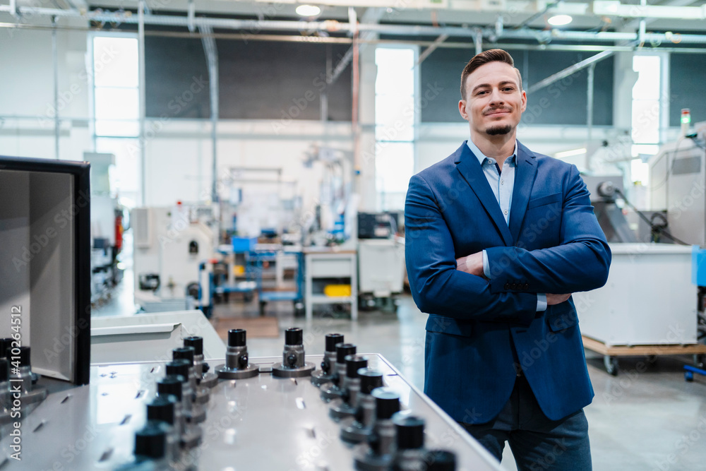 Smiling businessman with arms crossed by manufacturing equipment in factory Smiling businessman with arms crossed by manufacturing equipment in factory