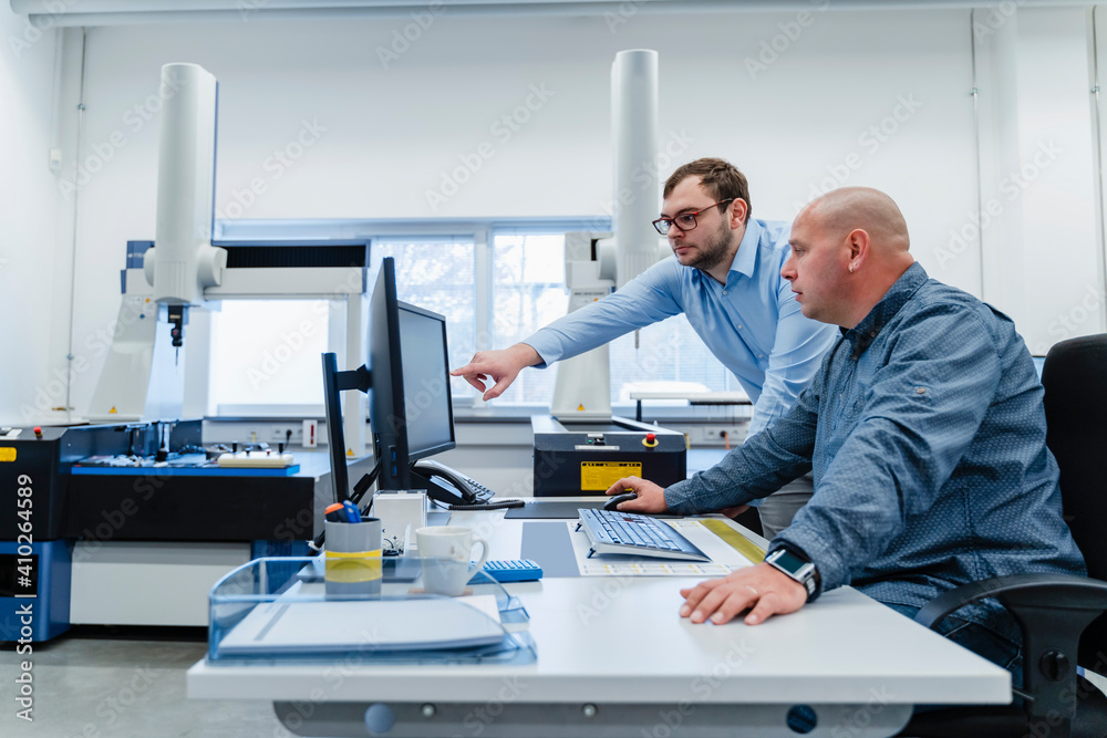 Male engineers working on computer while standing at office Male engineers working on computer while standing at office