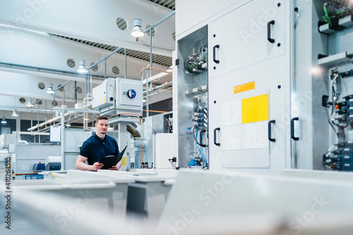 Male technician with file document surrounded by machines in factory photo