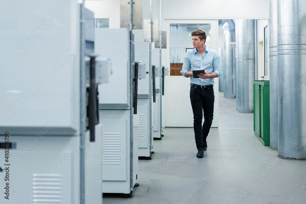 Young businessman holding digital tablet while walking by machinery equipment in factory Young businessman holding digital tablet while walking by machinery equipment in factory