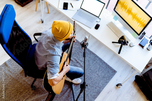 Male vlogger playing guitar while live streaming on camera at recording studio photo