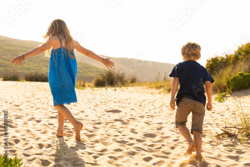 Brother and sister playing while walking on sand photo