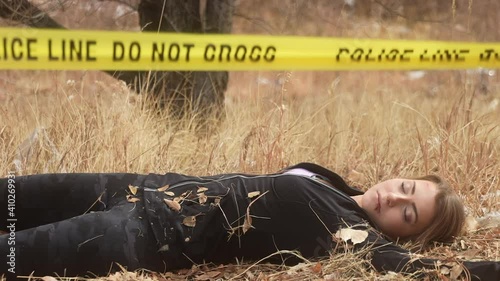 Detective approaches body of deceased female jogger and examines corpse for evidence behind police tape on grass field