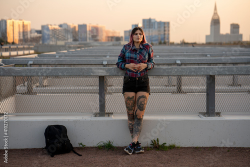 Fashionable woman day dreaming while leaning on railing at rooftop during sunset