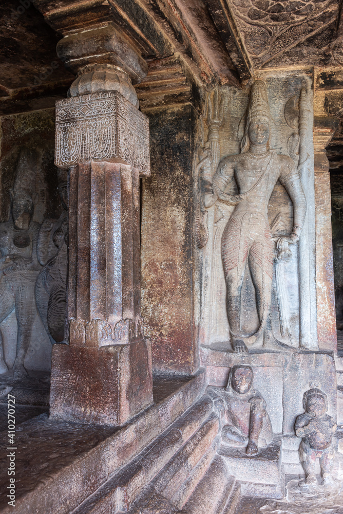 Aihole, Karnataka, India - November 7, 2013: Ravanaphadi Cave Shiva Temple. Gray-stone standing human figure sculptures, above a row of small figures. Aihole, Karnataka, India - November 7, 2013: Ravanaphadi Cave Shiva Temple. Gray-stone standing human figure sculptures, above a row of small figures.