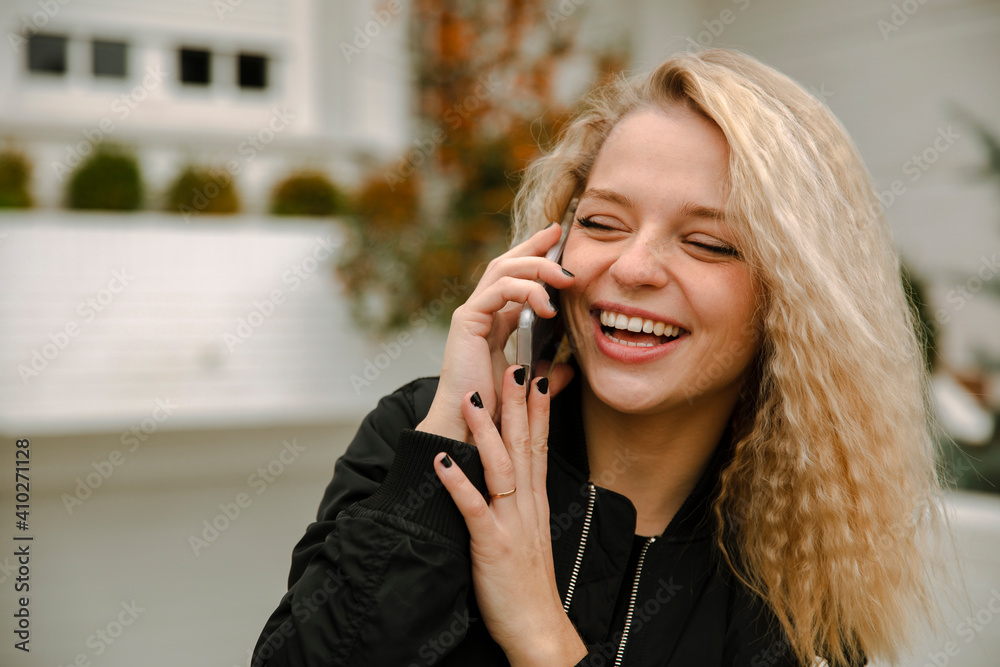 Hipster woman with eyes closed laughing while talking on smart phone in front yard Hipster woman with eyes closed laughing while talking on smart phone in front yard