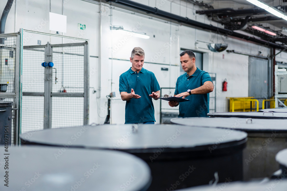Mature male engineer discussing with colleague about containers while walking in industry Mature male engineer discussing with colleague about containers while walking in industry