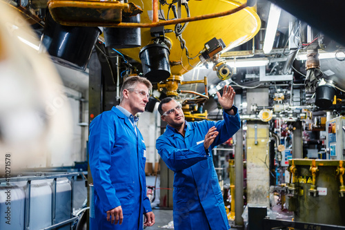 Male professionals discussing while examining manufacturing equipment in industry photo