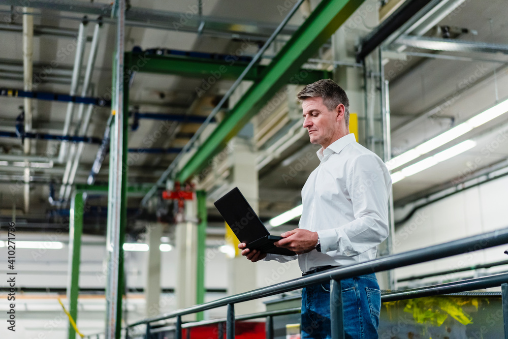 Mature male professional using laptop while standing in factory Mature male professional using laptop while standing in factory