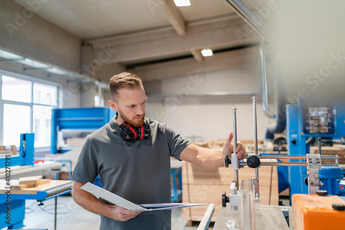 Portrait of carpenter inspecting machines in production hall with ring binder in hand photo