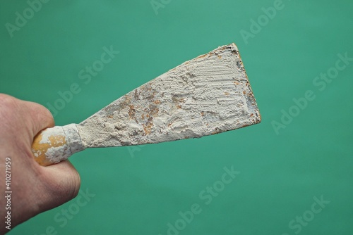 hand holds a dirty metal spatula in gray cement mortar on a green background