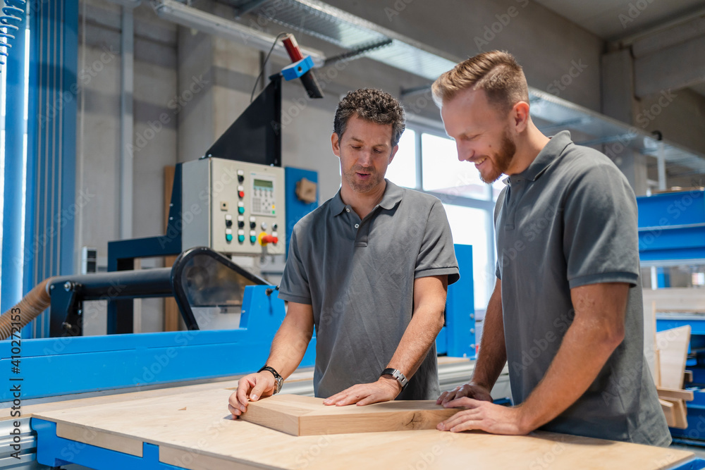 Two carpenters talking while examining wood in production hall Two carpenters talking while examining wood in production hall