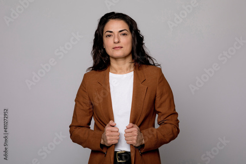 Woman with brown blazer jacket standing against gray background