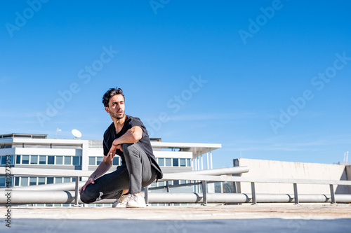 Handsome man looking away while crouching on rooftop during sunny day photo