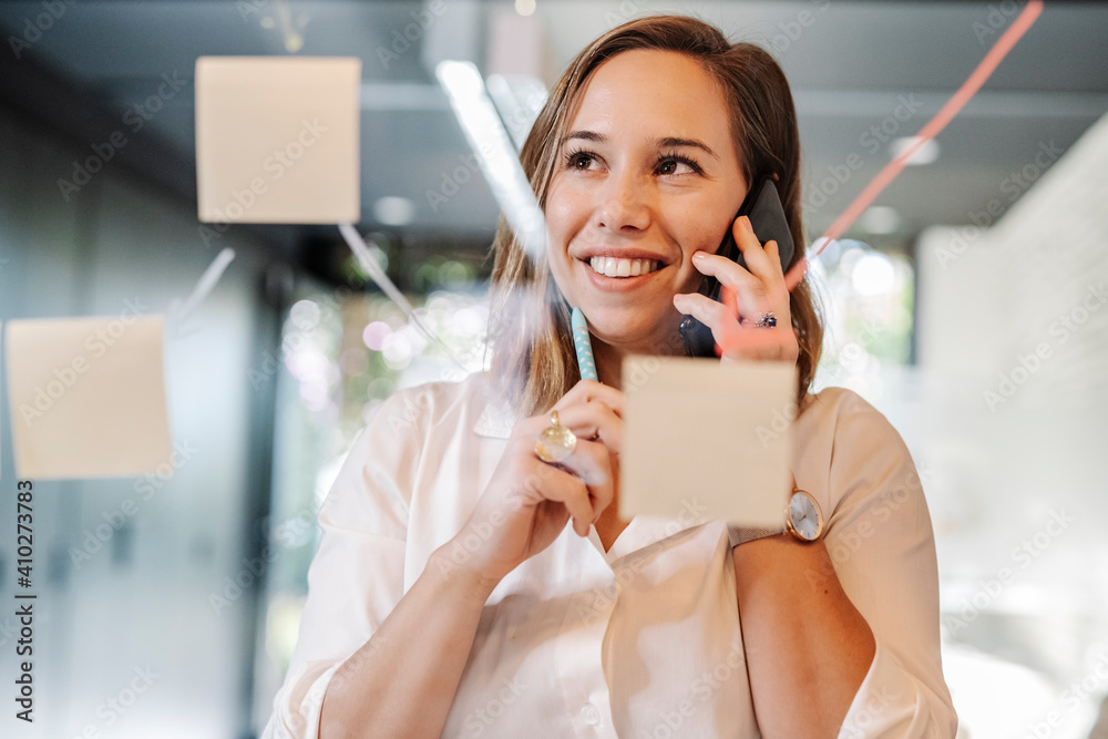 Close-up of smiling businesswoman talking over smart phone in office seen through glass wall