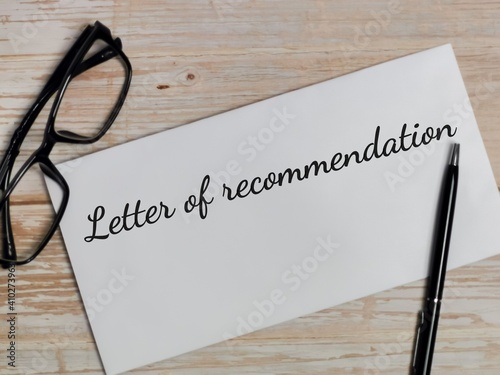Top view text Recommendation written on white envelope with pen and eye glasses on wooden table.