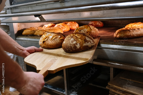 Male chef with pizza peel removing baked bread from oven at bakery photo